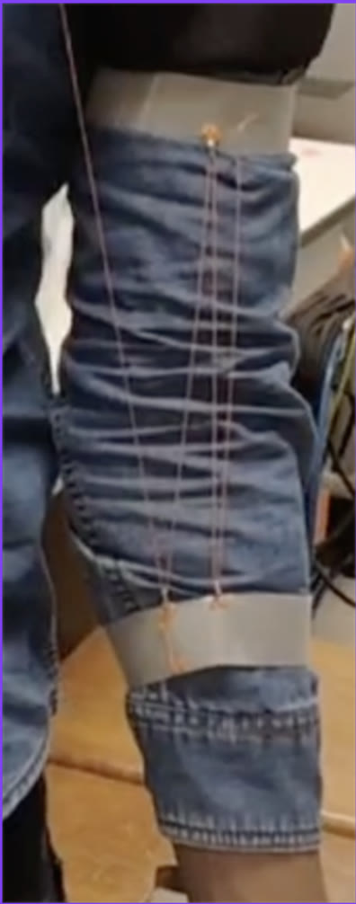 Close-up of a denim sleeve with two grey bands; orange fishing line runs in several parallel strands between hooks on the bands.