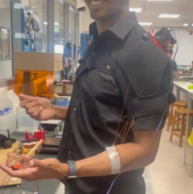 The prototype worn: a padded shoulder brace with the motor plate on top and fishing line running down to a white forearm band.
